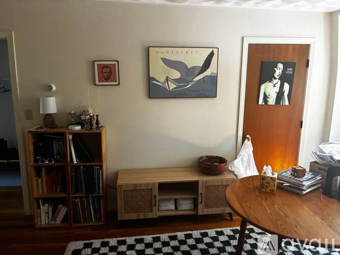 A living room with a bookshelf, a bench, a painting, and a door.
