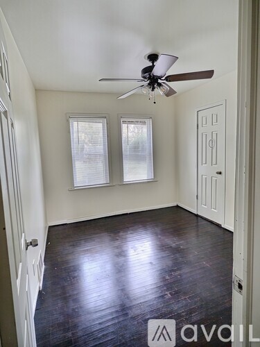 A room with a ceiling fan and two windows.