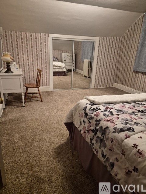 A bedroom with a bed, chair, and a dresser with a lamp on it.