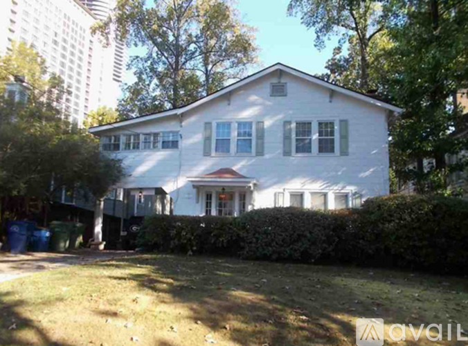 A white house with a red door and windows surrounded by trees and bushes.