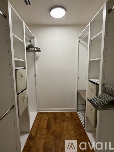 A small room with a wooden floor and white walls has a shelving unit and a hanging closet.