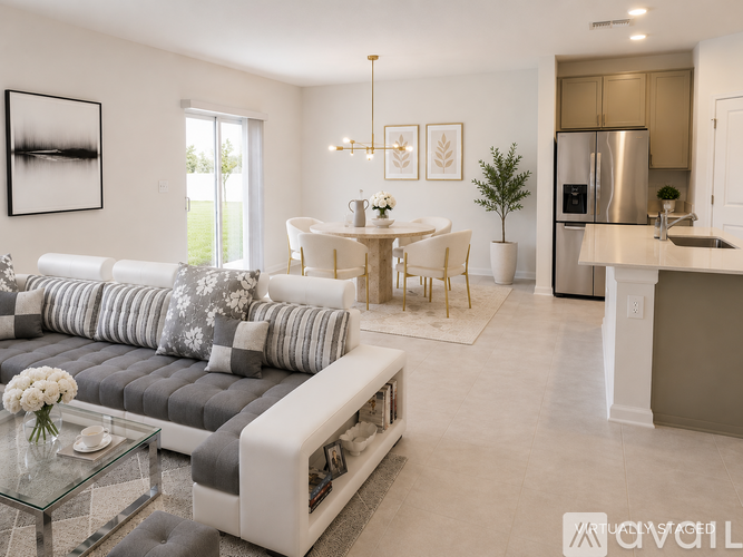 A modern living room with a grey and white sofa, a glass coffee table, and a kitchen area with a refrigerator and sink.