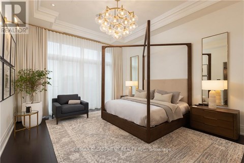 A bedroom with a four poster bed, a grey armchair, a side table with a lamp and a potted plant.