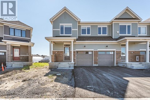 A real estate brokerage logo is displayed on a sign in front of a row of new houses.
