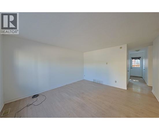A room with wooden flooring and white walls, with a doorway leading to another room.