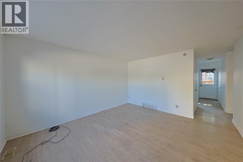 A room with wooden flooring and white walls, with a doorway leading to another room.
