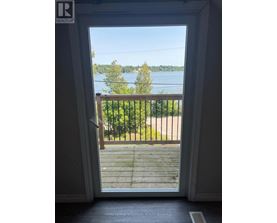 A doorway opens to a balcony with a view of a lake and trees.
