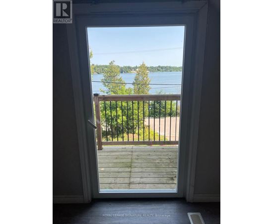 A doorway opens to a balcony with a view of a lake and trees.