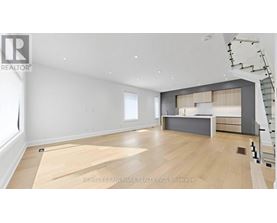 A spacious room with wooden flooring and a staircase on the right side.