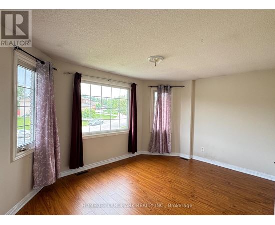 A room with wooden floors and two windows with curtains.