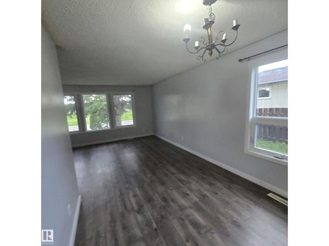 A room with a chandelier and wooden flooring.