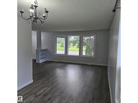 A room with a chandelier, wooden floors, and a large window overlooking a green area.
