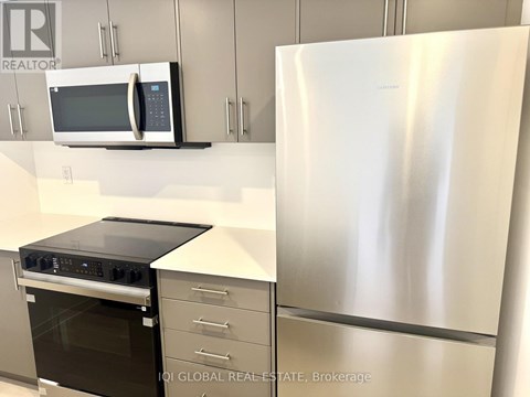A stainless steel refrigerator stands next to a microwave and oven in a kitchen.