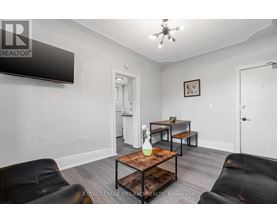A living room with a black leather couch, a wooden coffee table, and a flat screen TV mounted on the wall.