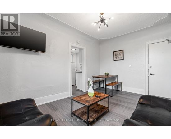 A living room with a black leather couch, a wooden coffee table, and a flat screen TV mounted on the wall.