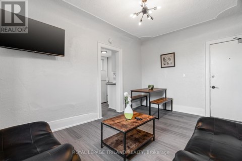 A living room with a black leather couch, a wooden coffee table, and a flat screen TV mounted on the wall.