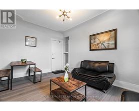 A living room with a black leather couch, a wooden coffee table, and a painting on the wall.