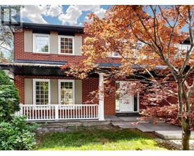 A red brick house with a white porch and a tree with orange leaves in front.