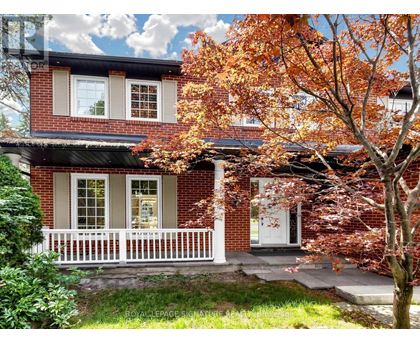 A red brick house with a white porch and a tree with orange leaves in front.