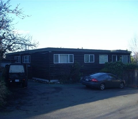 A black car is parked in front of a black house.