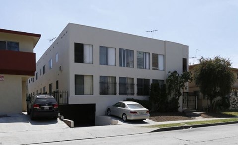 A white building with a black gate and two cars parked in front.