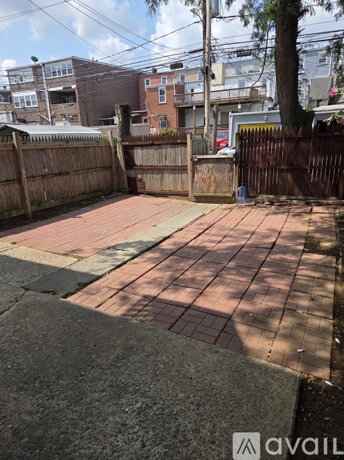 A brick walkway leads to a wooden fence and a tree.