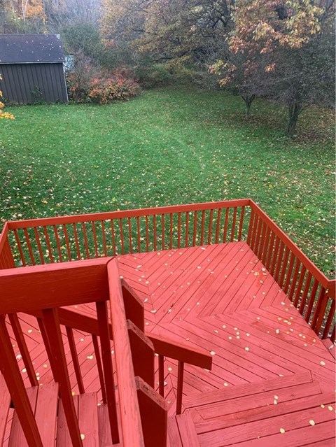 A red wooden deck with a railing and steps leading down to a grassy area.