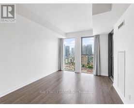 A spacious room with wooden flooring and a view of the city through the windows.