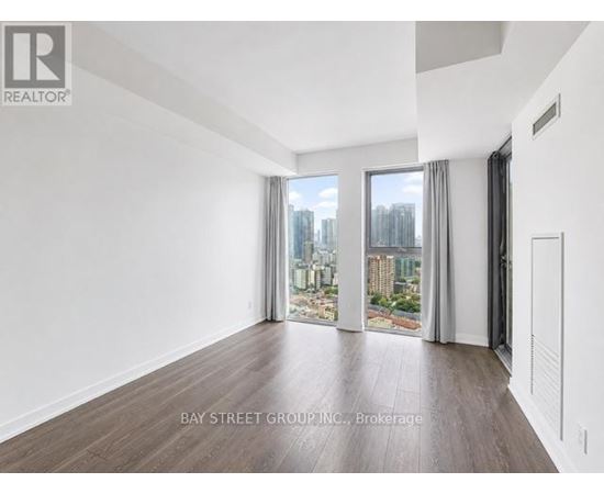 A spacious room with wooden flooring and a view of the city through the windows.