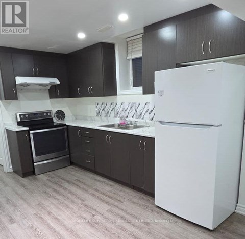 A white refrigerator stands in a kitchen with dark cabinets and a marble backsplash.