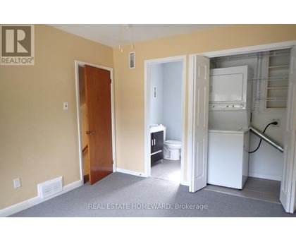 A room with a door and a kitchen area with a fridge and a toilet.