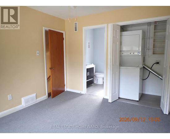 A room with a door and a kitchen area with a fridge and a toilet.