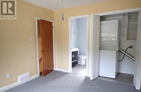 A room with a door and a kitchen area with a fridge and a toilet.