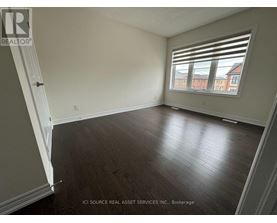 A room with wooden flooring and a window showing a view of a red building outside.