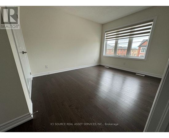 A room with wooden flooring and a window showing a view of a red building outside.