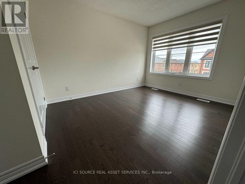 A room with wooden flooring and a window showing a view of a red building outside.