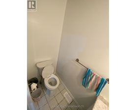 A white toilet with a white lid and a white trash can with a white trash bag in a white bathroom.