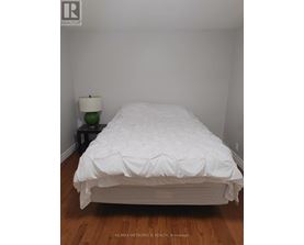A white bed with a white comforter and a white lamp with a green lampshade on a black table.