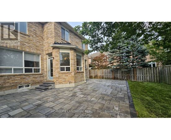 A stone patio leads to a brick house with a realtor sign.