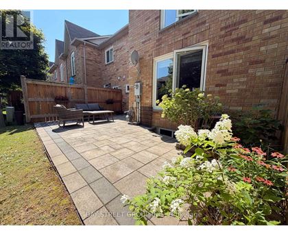 A backyard with a patio, a wooden fence, and a brick house.