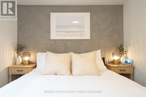 A bedroom with a large bed, two nightstands with lamps, and a framed picture on the wall.