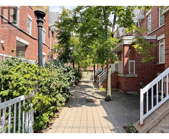 A tree-lined walkway between two rows of red brick houses.