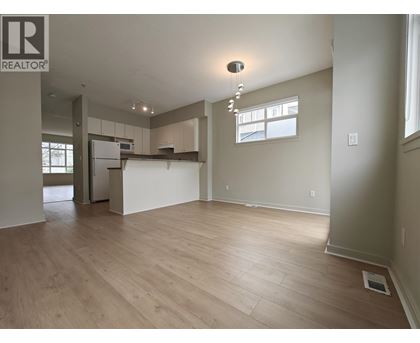 A spacious room with wooden flooring and a kitchen area in the background.