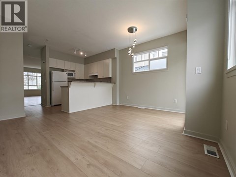 A spacious room with wooden flooring and a kitchen area in the background.