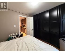 A bedroom with a bed in the foreground and a kitchen area visible through the open door.