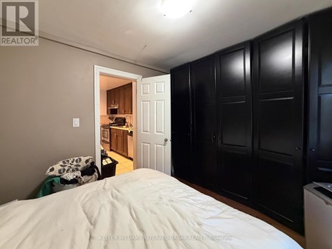 A bedroom with a bed in the foreground and a kitchen area visible through the open door.
