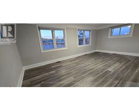 A room with wooden flooring and two windows.