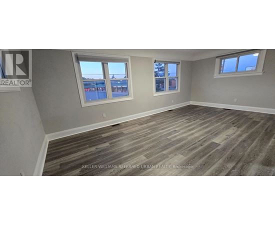 A room with wooden flooring and two windows.
