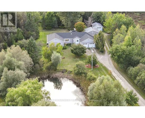A house with a grey roof is surrounded by greenery and a pond.