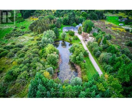 A bird's eye view of a house surrounded by trees and a pond.